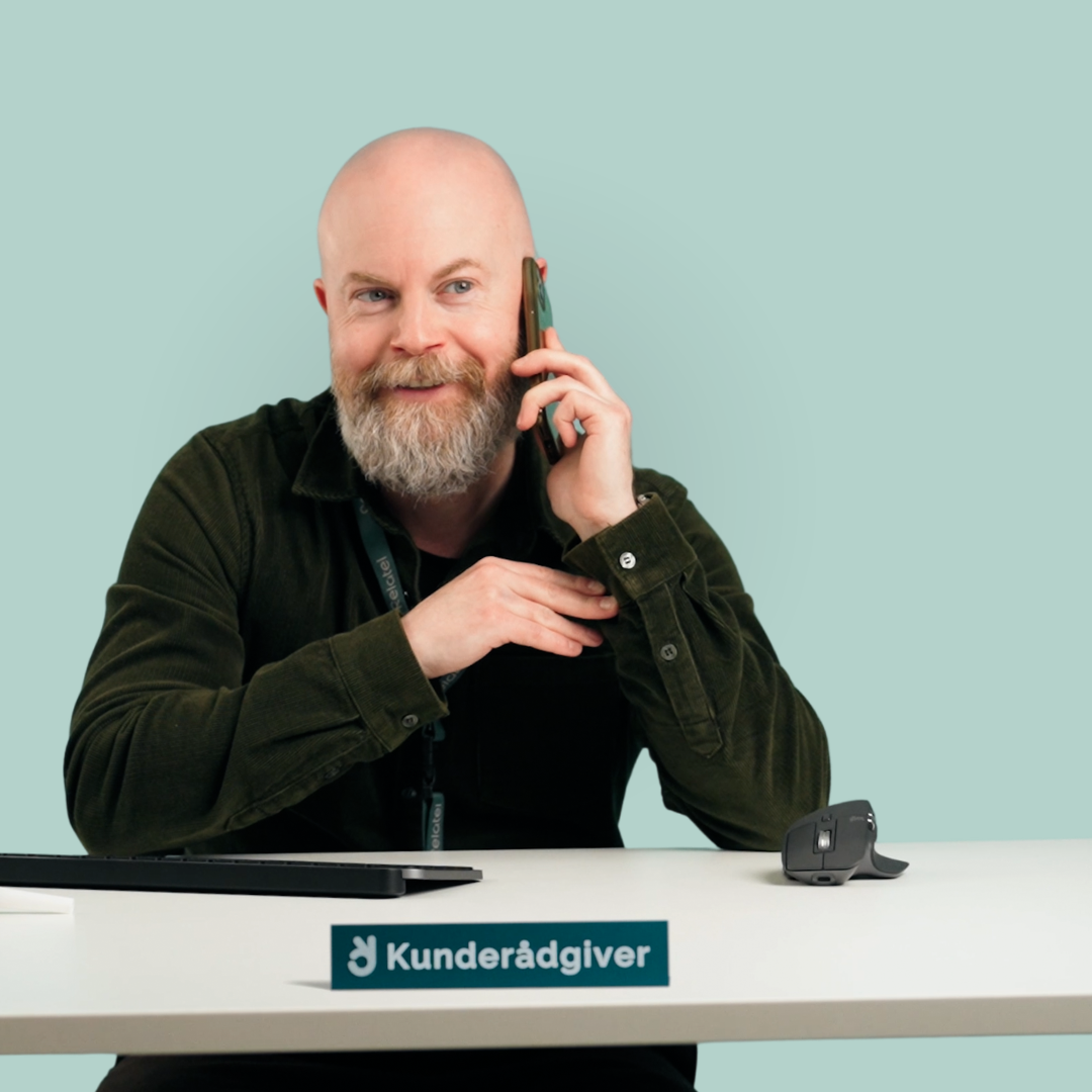 Mand taler i telefon som kunderådgiver ved et skrivebord